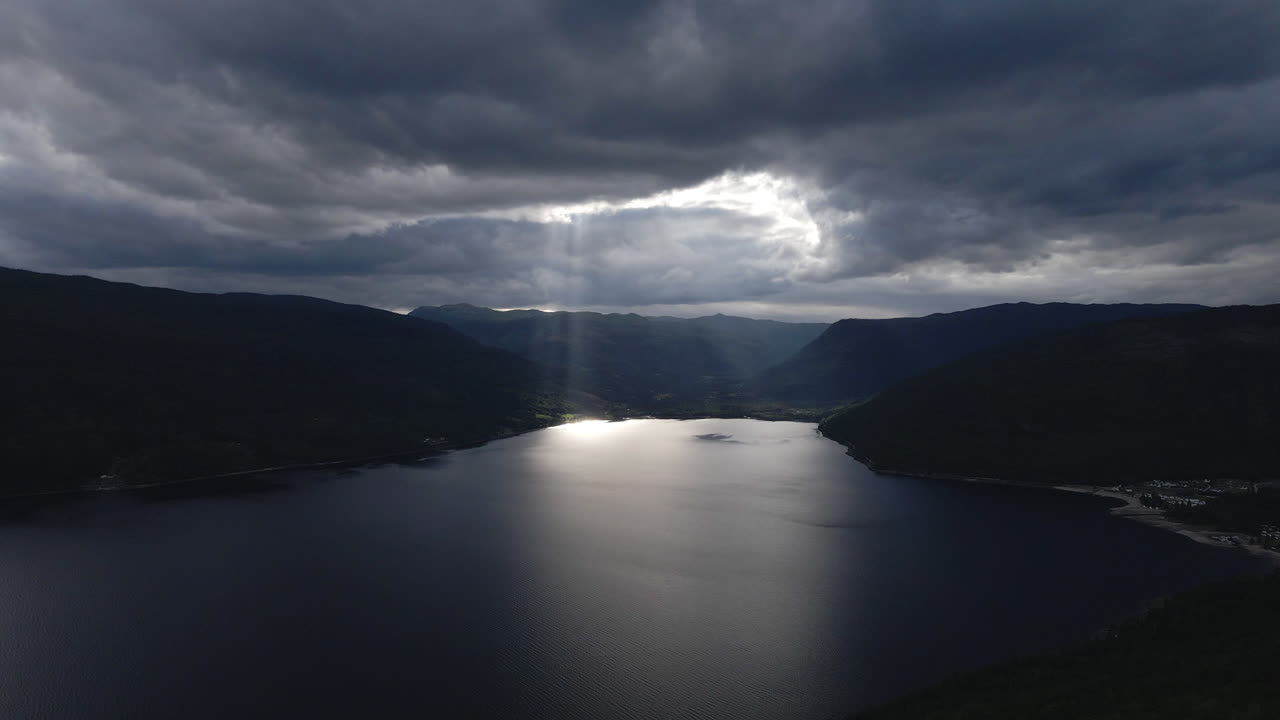 el dron captura el video de los rayos de luz que brillan desde un cielo nublado hacia un lago en una noche oscura y nublada