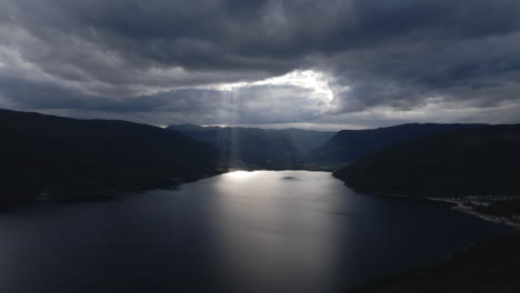 drone capture the video of the rays of light shine down from a cloudy sky into a lake on dark overcast evening