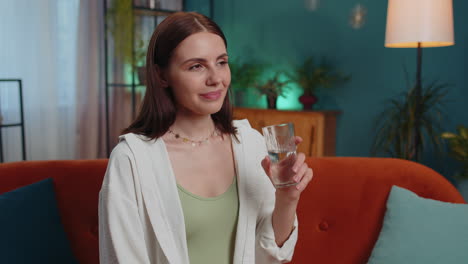 Thirsty-one-young-woman-sitting-at-home-holding-glass-of-natural-aqua-make-sips-drinking-still-water