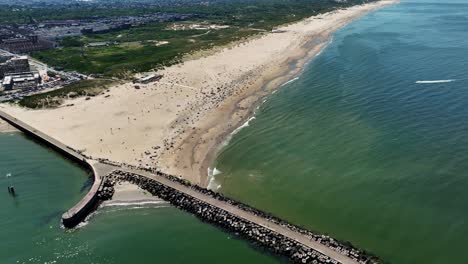 drone rises above beach on hot summer day with break water jetty protecting sand