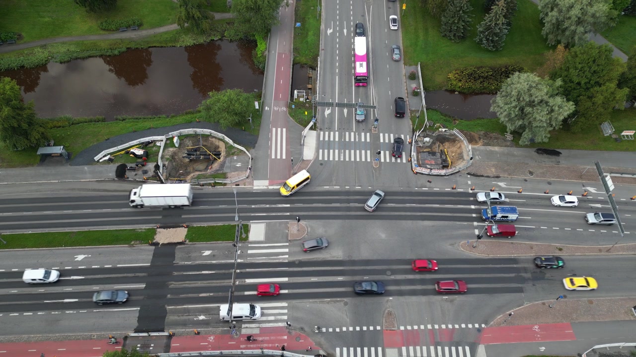 Bird's-eye view drone footage of vehicle traffic at an intersection in Raksila, Oulu, showing open trenches, pipes, and roadworks for a district heating reparation project.