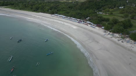 Waves-coming-into-shore-with-boats-and-green-trees-in-the-surrounding-area-in-Lombok,-Indonesia