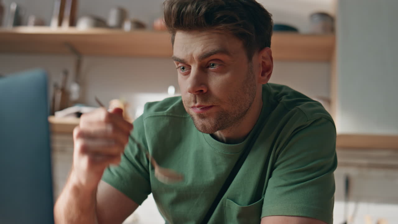 Eating guy looking computer enjoying breakfast in kitchen closeup. Man in home