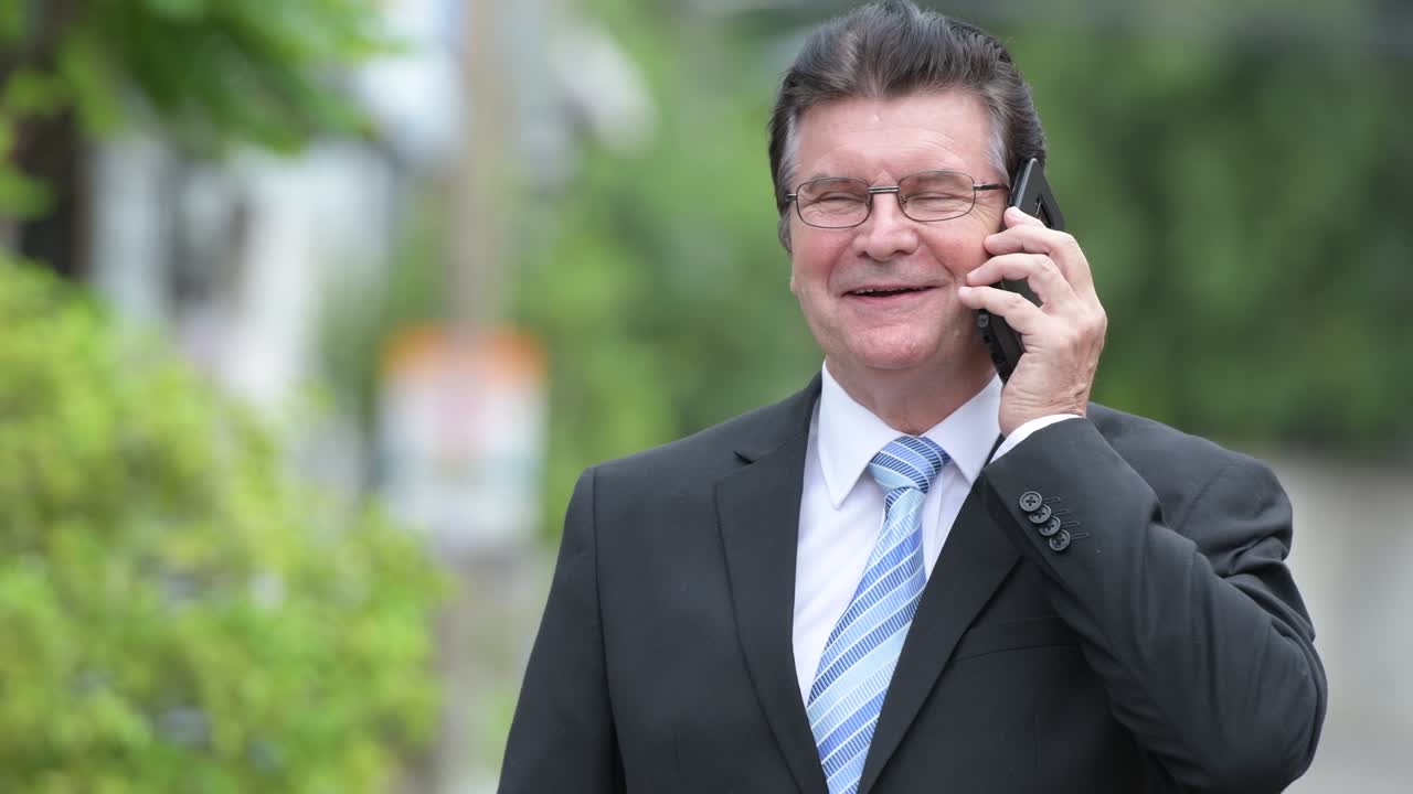 행복한 잘생긴 고위 사업가들이 거리에서 전화로 이야기하고 있습니다.