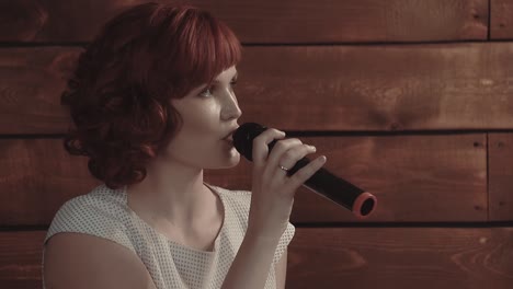 Young-girl-speaks-into-microphone-against-a-background-of-wooden-boards-close-up