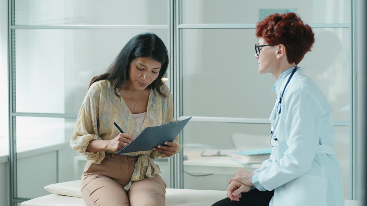 Hispanic Woman Signing Consent Form with Female Doctor in Clinic
