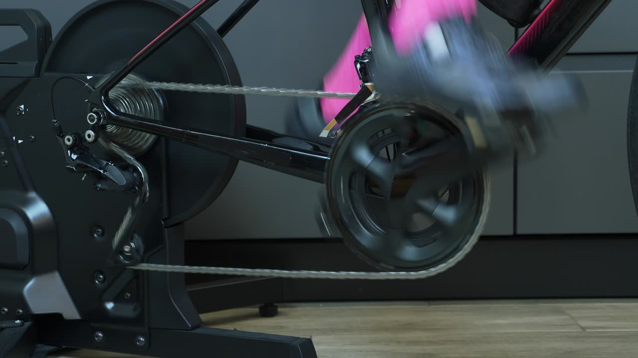 고정된 스마트 자전거 트레이너에서 페달을 는 여성 다리. 체인, 체인링, 집에서 스마트 고정 자전거 훈련. 자전거 컨셉. 후면 카세트와 함께 하인 및 체인링의 세부 사항