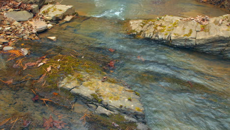 Close-up-of-a-creek-flowing-over-a-slick-rock-surface-past-leaves-and-small-stones-along-its-side