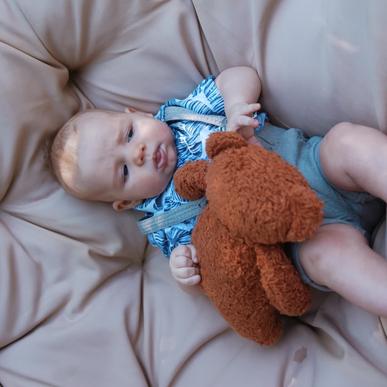 Un adorabile neonato caucasico è sdraiato in una sedia sospesa con un orsacchiotto. Un simpatico neonato si riposa all'aperto. Schermo verticale