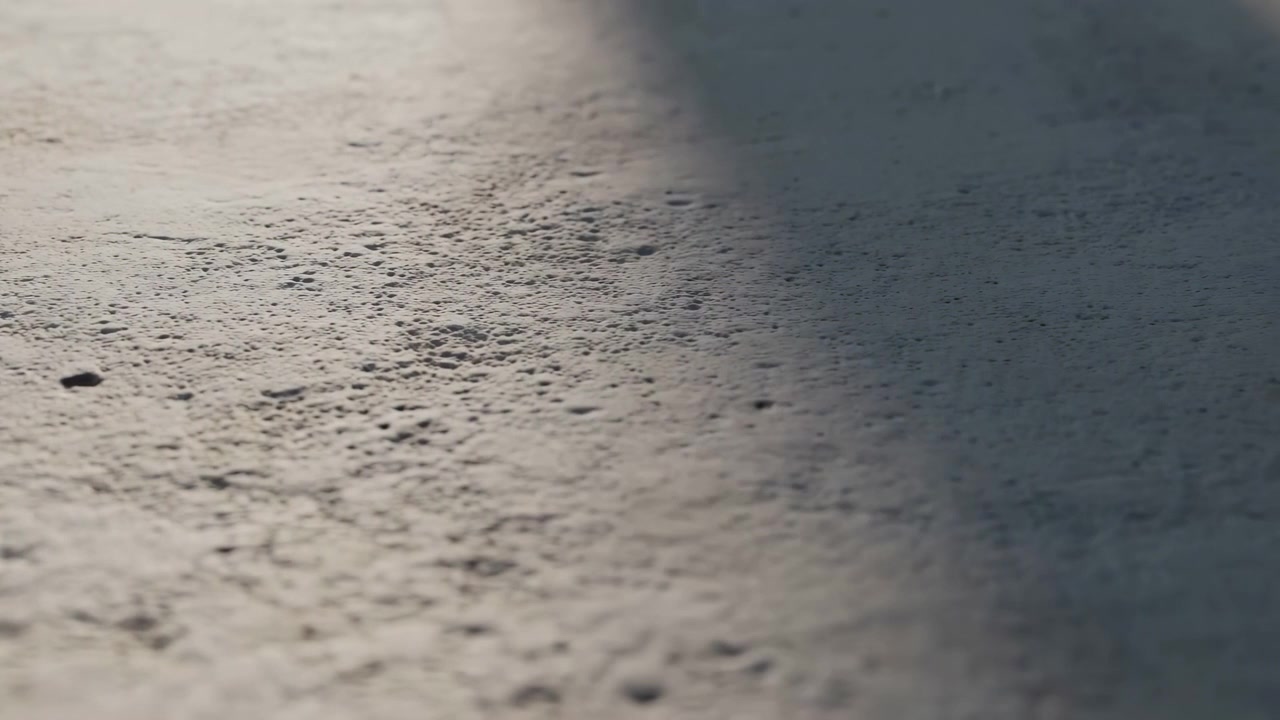小さな暗い斑点によって特徴づけられた、氷のような質感の表面のクローズアップを明らかにする中央フレーム。