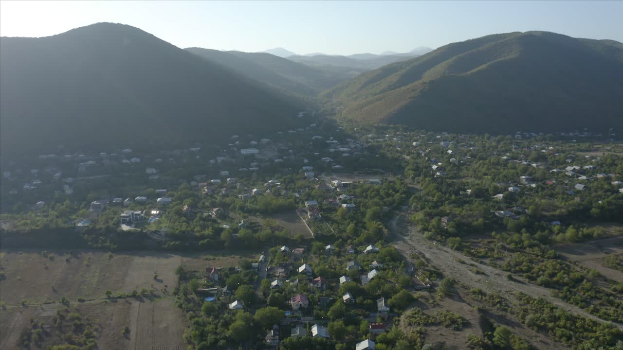 Revealing Shot Of Majestic Mountain Range By The Village In Georgia On A Bright Morning - aerial tilt-up