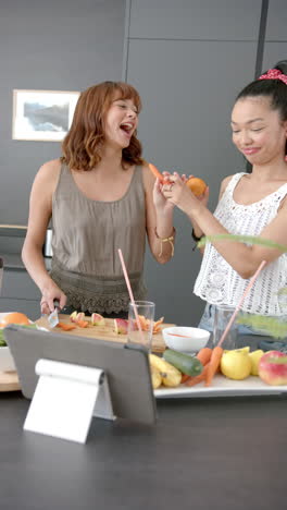 vertical video: preparing fresh juice, two women cutting fruits and vegetables in modern kitchen