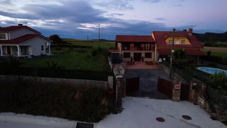 two rural homes with red roofs and a lush green yard at dusk in galizano, cantabria. aerial