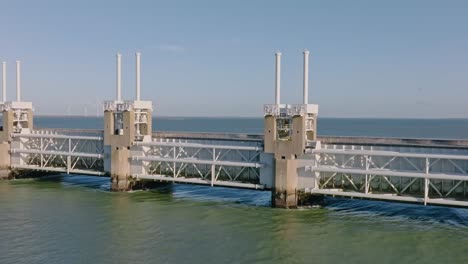 Aerial-shot-zooming-in-on-the-concrete-and-steel-front-of-the-Eastern-Scheldt-storm-surge-barrier-in-Zeeland,-the-Netherlands,-on-a-beautiful-sunny-day-with-blue-sky