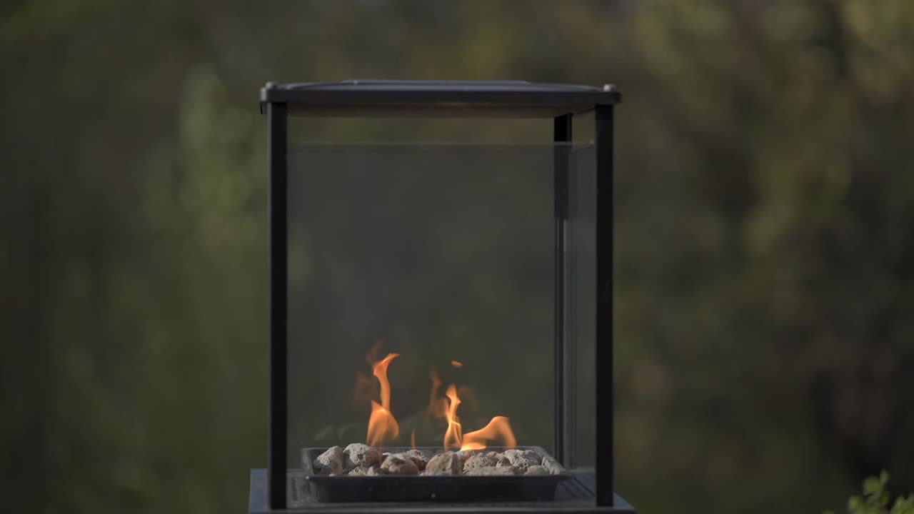 sleek, modern outdoor firepit with glass panels showcasing a warm flame over stones