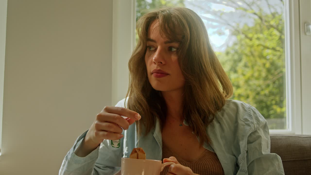 A Beautiful Woman is Deep in Thought as She Prepares a Cup of Tea on the Couch - Close Up