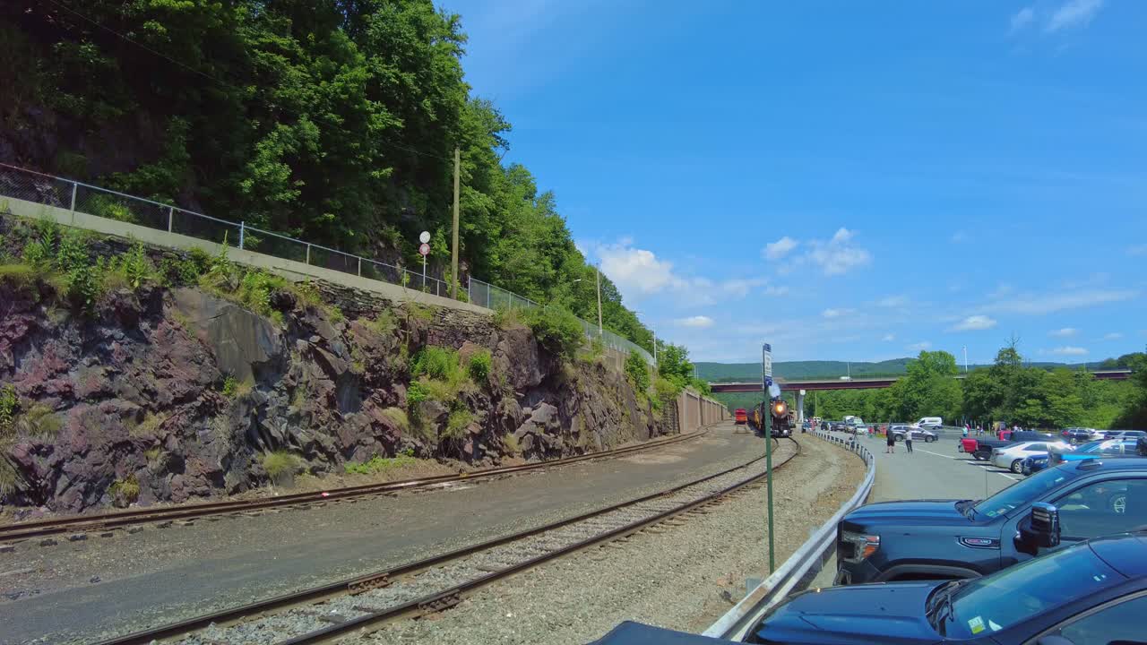 Witness a beautiful steam locomotive as it journeys through a picturesque mountain valley, surrounded by lush greenery and rocky terrain in the warm afternoon light.