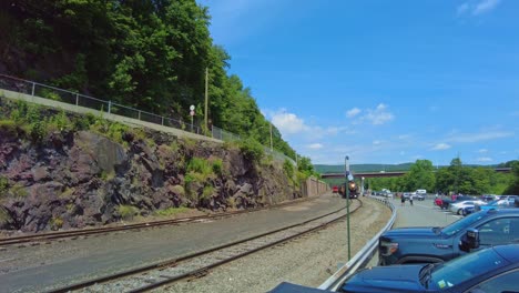 witness a beautiful steam locomotive as it journeys through a picturesque mountain valley, surrounded by lush greenery and rocky terrain in the warm afternoon light.