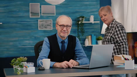 Senior man looking at camera smiling sitting in workplace at desk