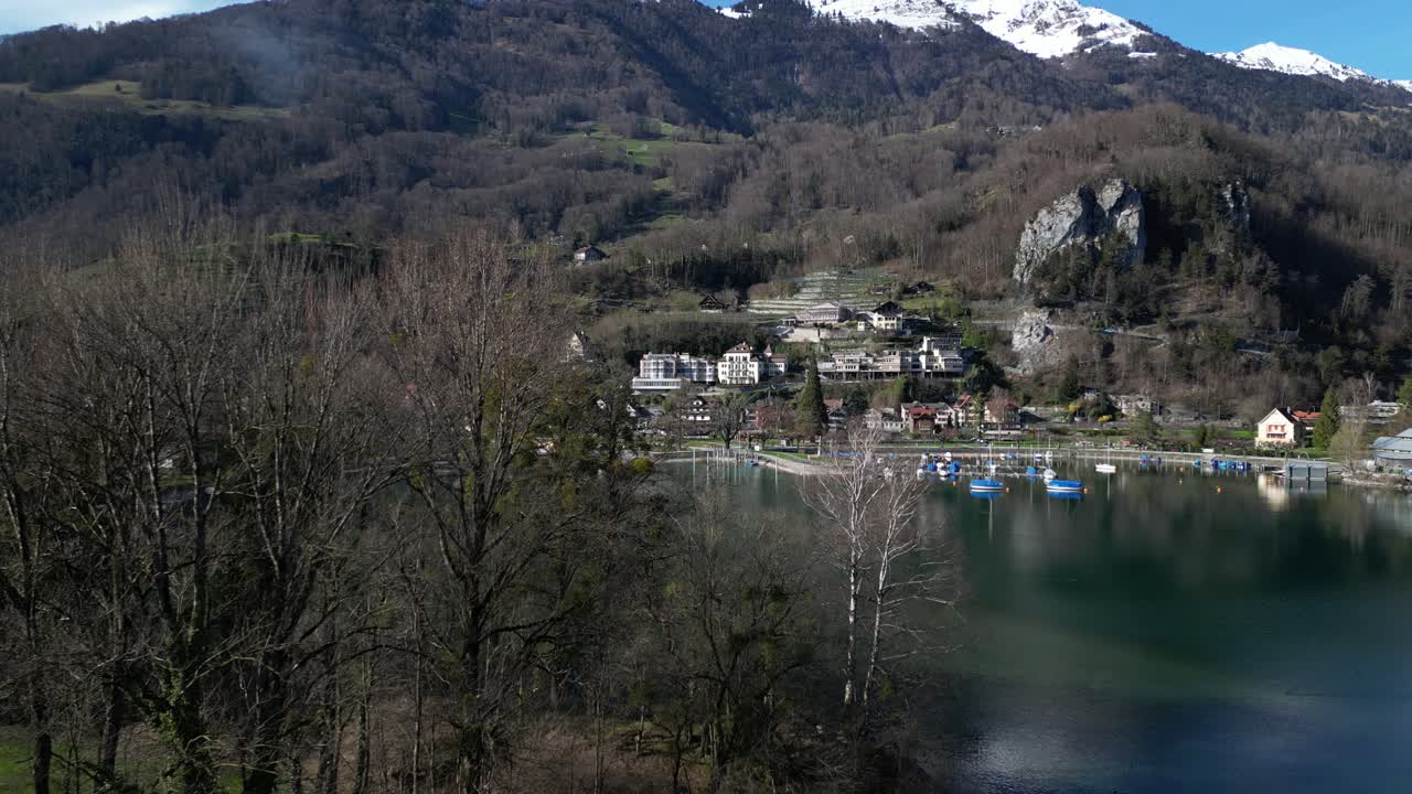 clip de avión no tripulado que muestra un puerto de pequeños barcos en un lago tranquilo, con una cordillera cubierta de nieve en el fondo