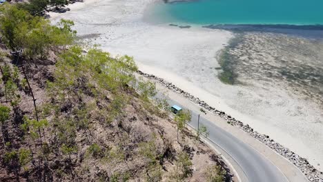 Aerial-view-of-blue-bus-driving-along-a-scenic-coastal-road-in-the-capital-city-of-Dili,-Timor-Leste,-Southeast-Asia