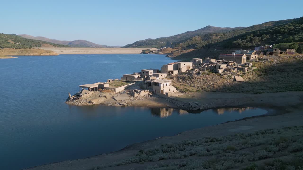Cinematic aerial view of the abandoned village of Sfendili on the shores of Aposelemis Lake in Crete, with the impressive dam framed in the scenic Mediterranean background