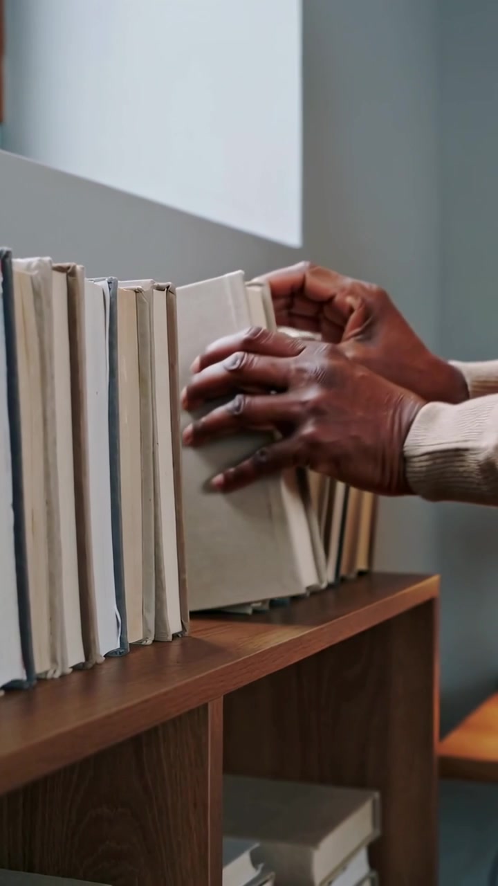 Vertical video: Sliding into row, aged hands in beige pinching cloth books at home, tidying shelf
