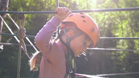 young girl challenging herself in climbing park - beautiful sun backlight with solar flare and girl moving ahead in slow motion - 6 year old female european with safety equipment