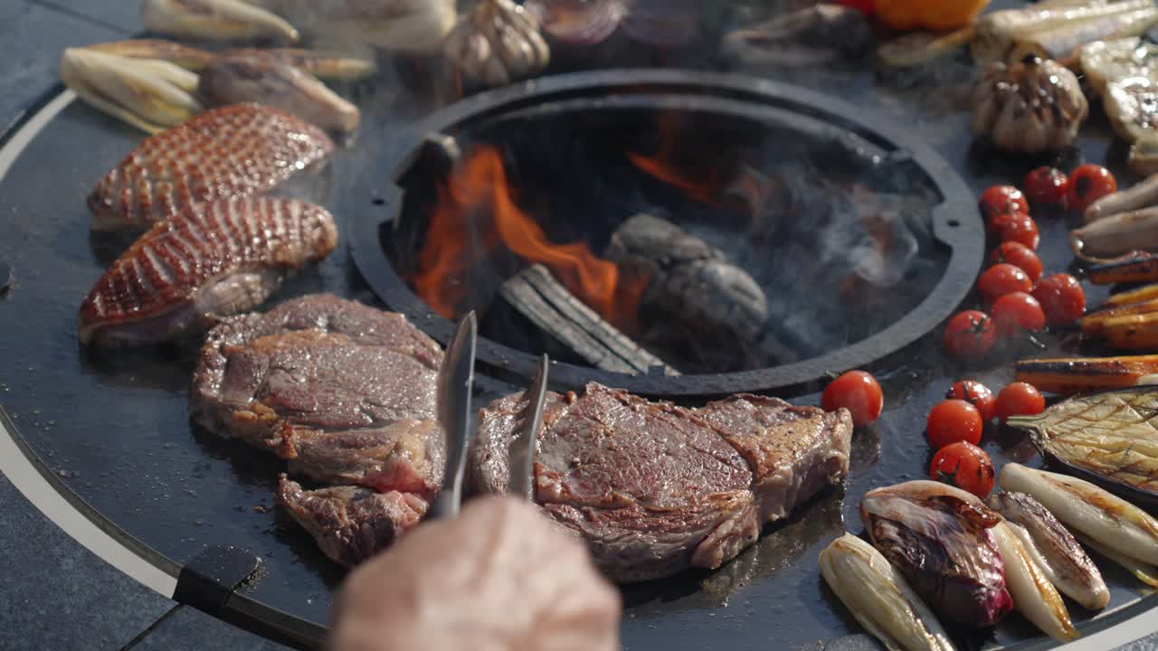 slowmotion shot of a chef tending to the various meats and food being cooked