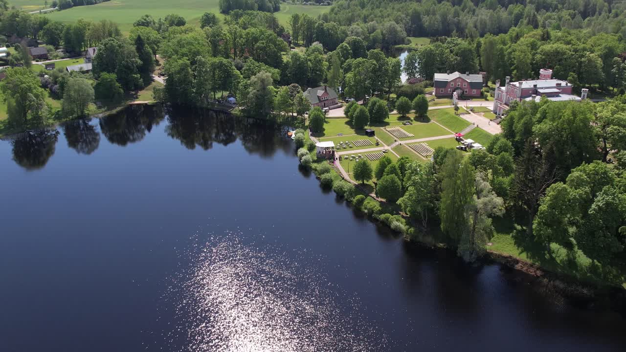 Aerial view of the small town of Birini Castle, located in a green park. The parish is surrounded by well-maintained paths, trees and open grass. Residential buildings and a lake