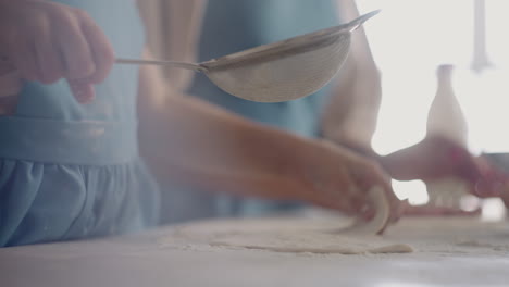 little girl is helping mother during cooking pie or bun daughter is kneading dough and pouring flour closeup