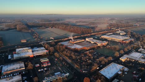 frozen rooftops of company and factory during golden sunrise in industrial area. traffic on highway and snowy farm fields in distance. aerial wide shot.