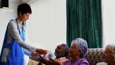 Side-view-of-Caucasian-female-doctor-serving-coffee-to-senior-people-in-nursing-home-4k