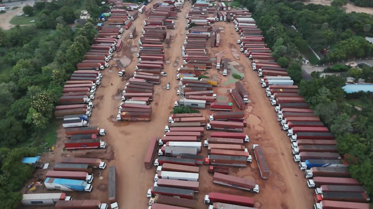 A powerful aerial view capturing the heart of a major logistics hub. Hundreds of freight trucks stand idle in a sprawling yard, representing a critical pause in the relentless movement of goods