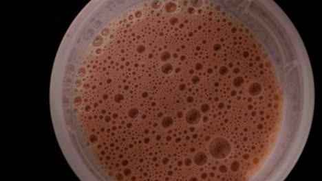 static shot of a bubbly chocolate-flavored fitness protein shake against a black background