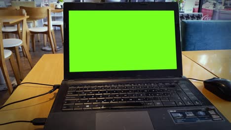 laptop computer with green screen over a wood table in a cafeteria.