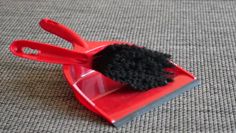 red plastic dustpan with brush on grey carpet