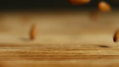 close up shot of almond nuts dropping onto wooden surface against black studio background shot in slow motion 2