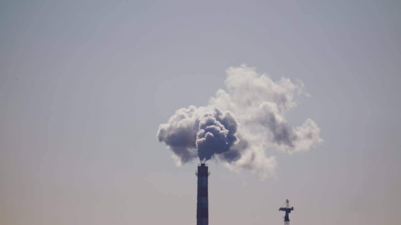 Ciminiera industriale che rilascia fumo denso nel cielo sopra un cantiere edile cittadino.