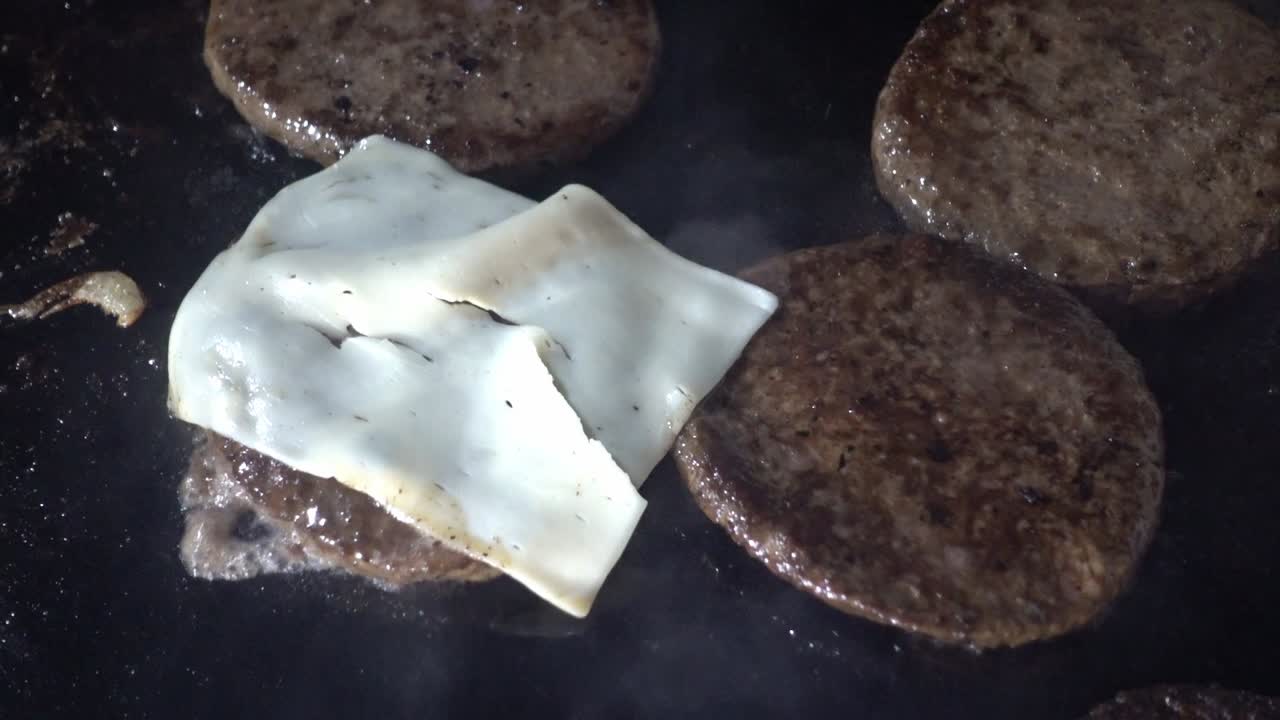 disparo en primer plano de rebanadas de queso que se agregan a las hamburguesas de carne en una parrilla