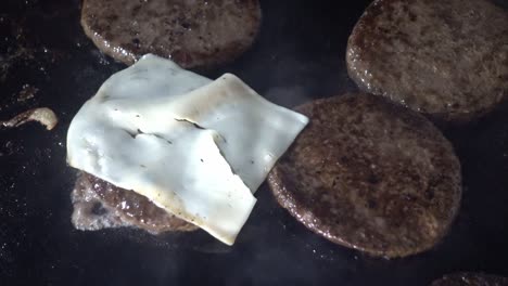 disparo en primer plano de rebanadas de queso que se agregan a las hamburguesas de carne en una parrilla