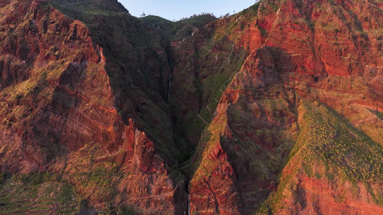 Scenic Paul do Mar waterfall down cliff face and shelter harbor, aerial reveal
