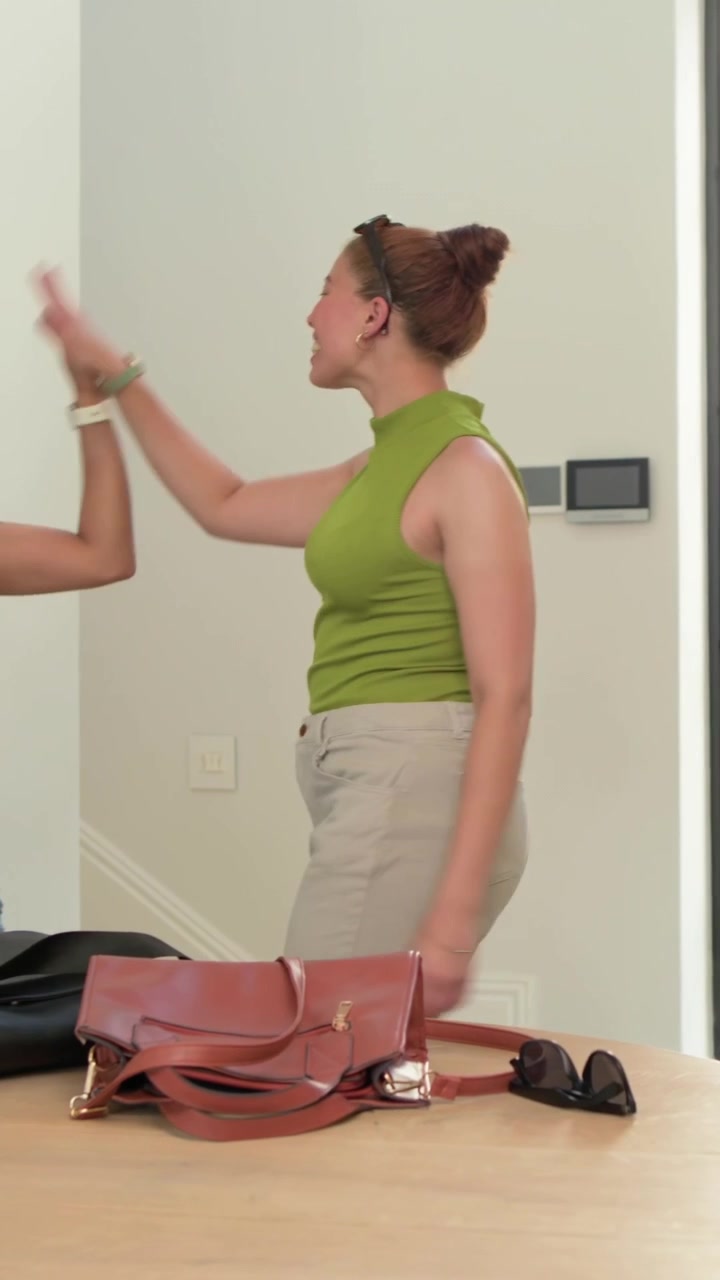 Vídeo vertical: Portas se abrindo, mulher de blusa verde carregando bolsa preta, colocando o celular, visitando uma casa.
