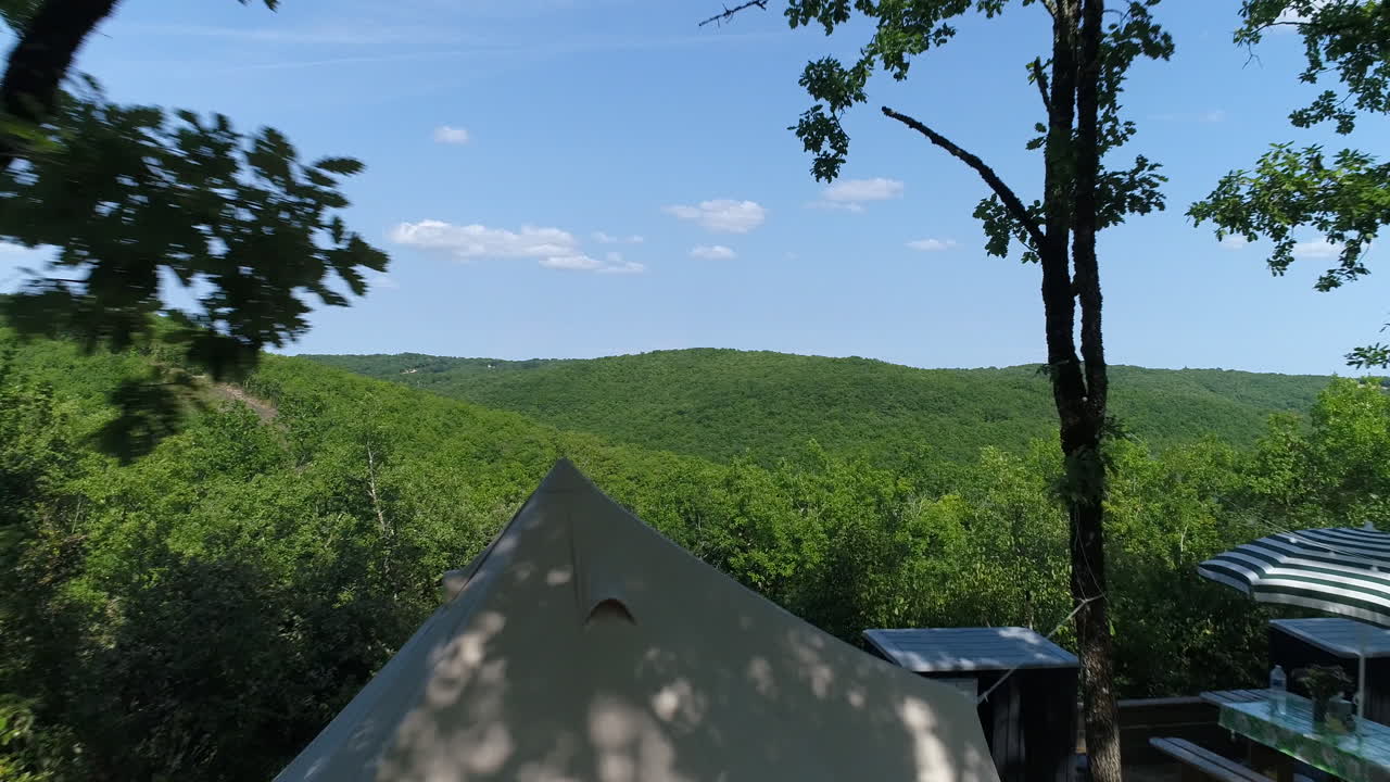 텐트와 티피가 있는 캠핑장 위를 날아다니며 숲을 발견합니다.