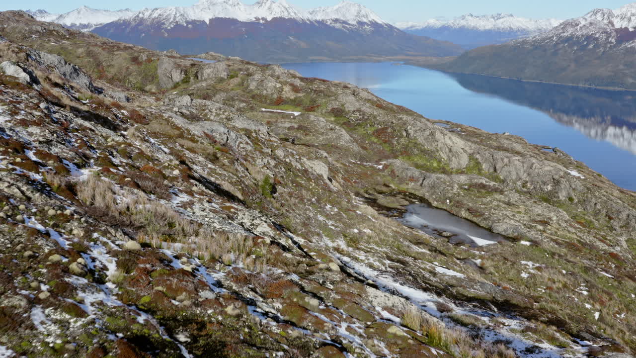 Rocky coastline with jagged cliffs and sparse vegetation along Cape Horn terrain, aerial dolly over rugged mountain icy landscape