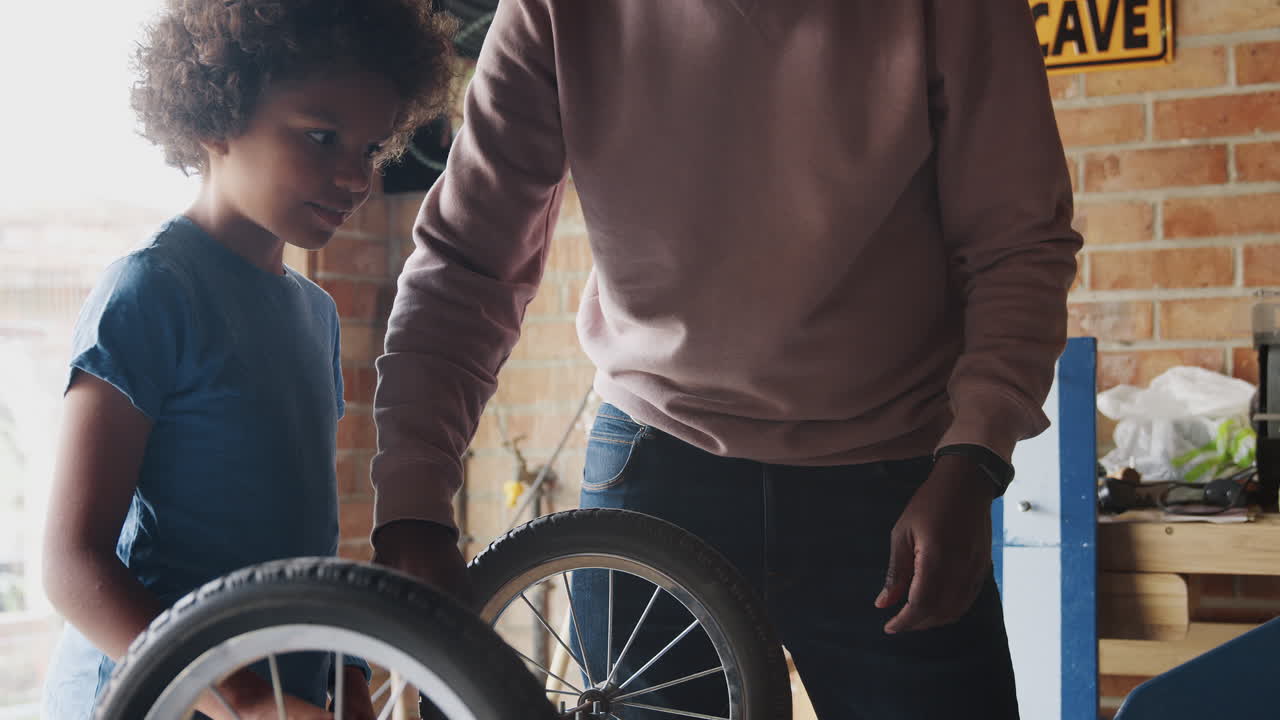 padre negro de mediana edad y su hijo preadolescente de pie en un banco de trabajo construyendo un kart de carreras juntos en su garaje, de cerca, sección media del padre