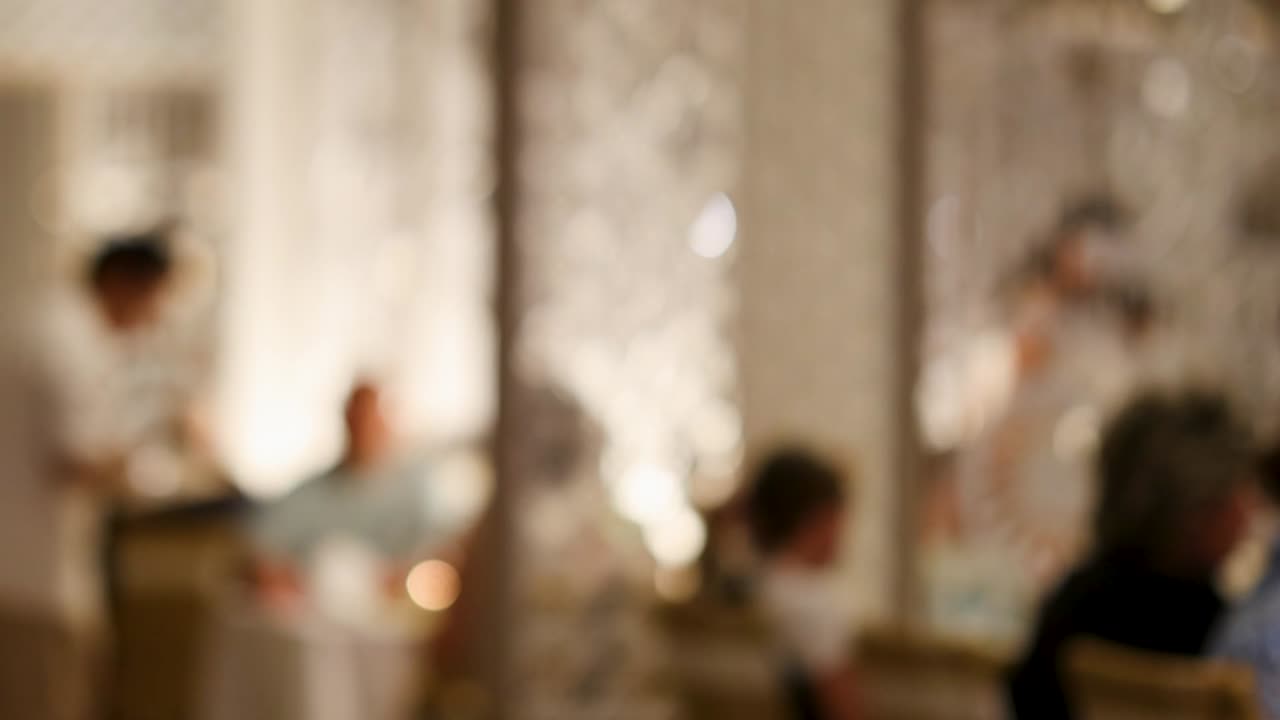 A softly blurred view of a restaurant with a waiter attending to seated guests, creating a cozy atmosphere.