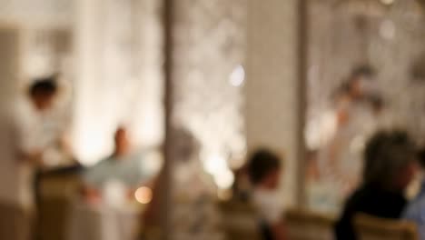 a softly blurred view of a restaurant with a waiter attending to seated guests, creating a cozy atmosphere.
