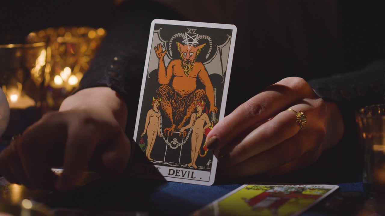 primer plano de una mujer dando una lectura de cartas del tarot en una mesa a la luz de las velas sosteniendo la carta del diablo 5