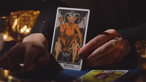 close up of woman giving tarot card reading on candlelit table holding the devil card 5